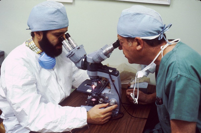 Two doctors in PPE looking at microscopes.